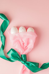 White Easter eggs in a bouquet with a green ribbon on pink background