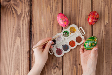 Close-up of woman's hands painting an easter egg on wooden background