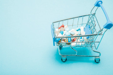 Pills and Shopping trolley on blue background. Creative idea for health care cost, drugstore, health insurance and pharmaceutical company business concept. Copy space