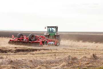 Obraz premium Agriculture,tractor preparing land with seedbed cultivator as part of pre seeding activities in early spring season of agricultural works at farmlands