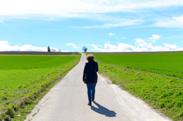 Woman walking away along a road through fields