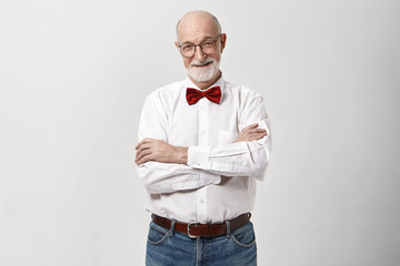 Studio shot of cheerful handsome grandfather with beard and bald head smiling, keeping arms crossed...