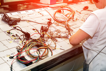 Hands of employees who check the quality of the wiring for cars at a modern plant on a special...