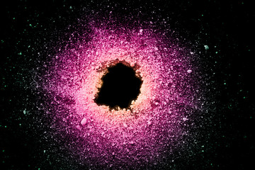 An explosion of pastel natural colored pigment powder on black background. Purple green yellow  particles textured background.