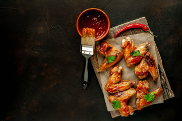 Grilled chicken wings in a barbecue sauce with parsley on a cutting board on a concrete table. Top...