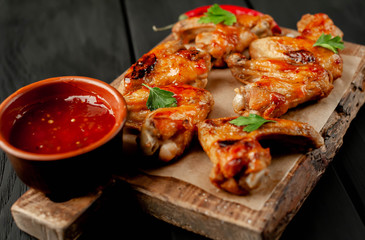 Grilled chicken wings in a barbecue sauce with parsley on a cutting board on a wooden background