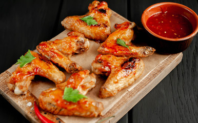 Grilled chicken wings in a barbecue sauce with parsley on a cutting board on a wooden background