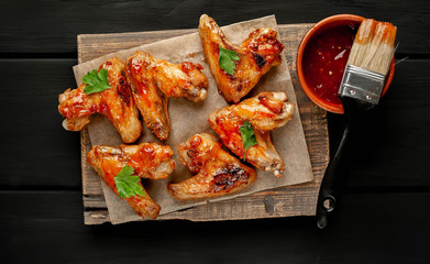 Grilled chicken wings in a barbecue sauce with parsley on a cutting board on a wooden background