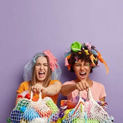 Two mad interracial volunteers busy with seperate waste collection and recycle, hold net garbage...