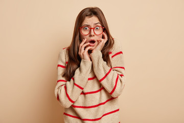 Headshot of scared frightened beautiful woman looks nervously at camera, keeps both hands near...