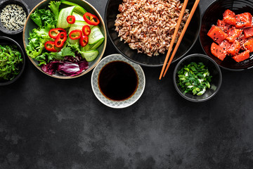 culinary background of poke bowl ingredients - brown rice, trout or salmon fillet, Chuka Seaweed Salad, sesame and fresh vegetables, top view, copy space, healthy food background