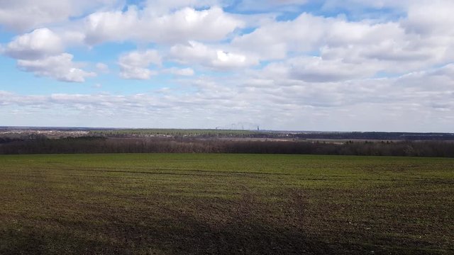Eastern Europe panorama fields of early spring. Sunny cloudy weather. Countryside. Industrial enterprise buildings in the background.