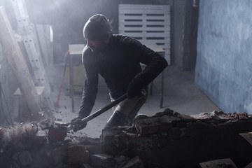 A man handyman breaks a brick wall with a hammer, builds and repairs his house
