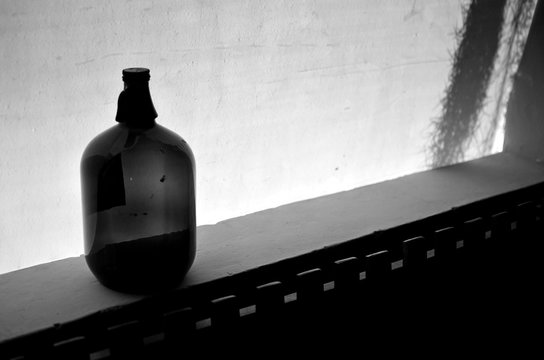 Botella a contraluz. Botella antigua a contra luz. Botella colocada sobre pared. Contraluz de cortina y botella. 