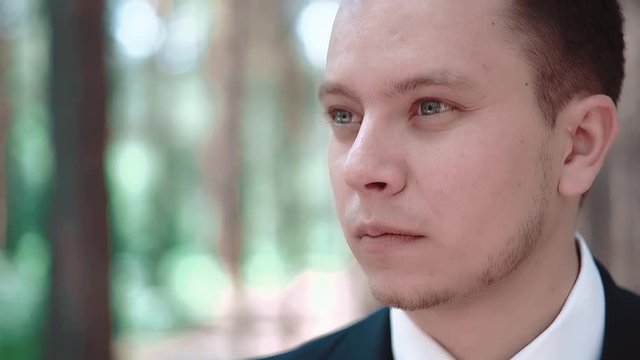 Young man standing among trees and looking afar, portrait, close-up