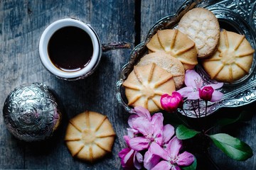 tasty coffee in a traditional Turkish cup and butter cookies and a sprig of pink flowers on a wooden table - flat lay food background