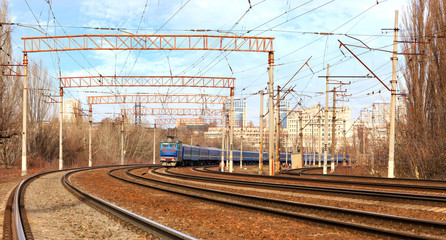 Fototapeta na wymiar Passenger train cars of the train ride on the railway tracks in the background of the cityscape