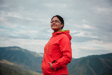 Naklejka premium Girl smiling in a red jacket sitting on the mountain. Enjoys the beautiful view around.