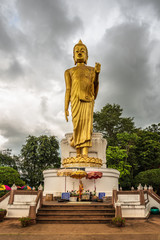 Buddha in the storm. A standing golden buddha statue against a stormy sky near the border point where the Mekong river leaves Thailand to enter Laos -  (Phra Yai Phu Khok Ngio)