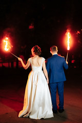 Fototapeta na wymiar beautiful young newlywed couple with fire torches in their hands and fireworks 1