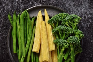 Fresh baby corn, broccolini and green beans vegetables isolated on dark background with copy space for your text