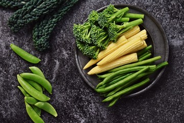 Fresh baby corn, broccolini and green beans vegetables isolated on dark background with copy space for your text