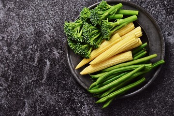 Fresh baby corn, broccolini and green beans vegetables isolated on dark background with copy space for your text