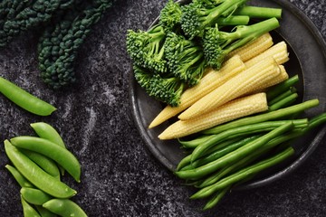 Fresh baby corn, broccolini and green beans vegetables isolated on dark background with copy space for your text