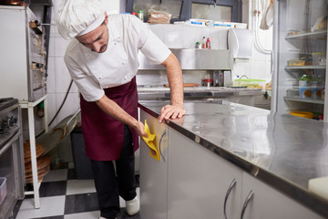 young chef in kitchen wiping cabinets, after closing restaurant.