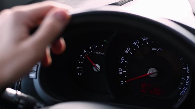 Young man standing on the parking, presses the accelerator pedal. The camera is aimed at the steering wheel with hand on it and on the cars dashboard.