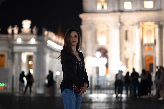 Beautiful girl with amazing long hair and red lips walking in the city at night. Pretty girl with adorable eyes posing on the background of night architecture
