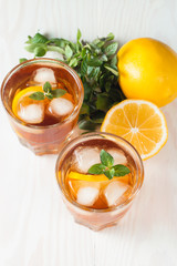 Refreshing citrus lemonade, summer drink. Ice tea with fresh lemon and mint on wooden background. Refreshment beverage concept.
