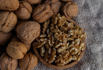Walnuts in wooden round bowl, and walnuts with shell on sack surface