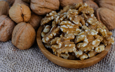 Walnuts in wooden round bowl, and walnuts with shell on sack surface