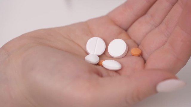 Close-up view of young woman's hand holding vitamins and minerals pills. She is choosing and taking yellow ones
