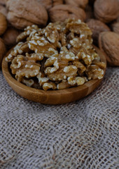 Walnuts in wooden round bowl, and walnuts with shell on sack surface