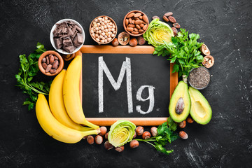 Foods containing natural magnesium. Mg: Chocolate, banana, cocoa, nuts, avocados, broccoli, almonds. Top view. On a black background. - obrazy, fototapety, plakaty