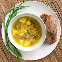 a bowl of beef and vegetables soup served with green onion and bread