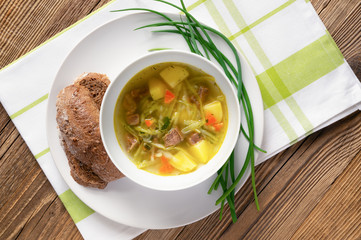 soup of cabbage, beef, carrot, and onion with green herbs and bread served on napkin on rustic surface