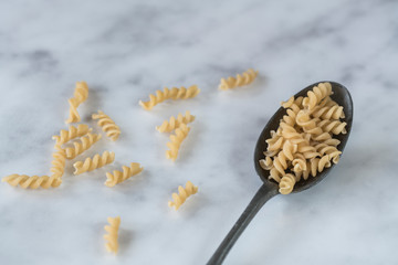 flat lay vintage dark silver spoon with heap pasta spiralli, fusilli, on white grey marble kitchen...