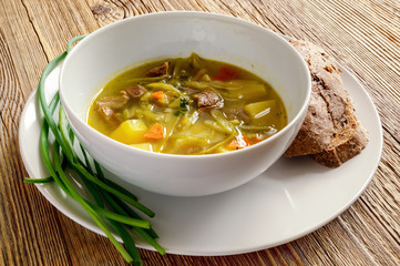 shchi served with bread and green onion on wooden table