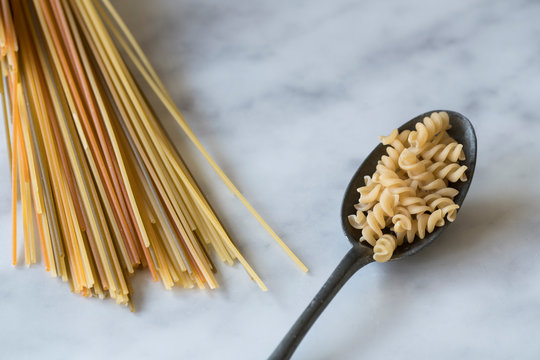 flat lay vintage dark silver spoon with heap pasta spiralli and spaghetti on white grey marble kitchen dresser