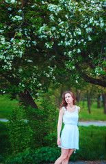 Naklejka premium beautiful woman with brunette hair in white dress posing on a background of blooming apple trees