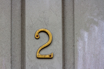 House number two with the 2  in old bronze on a dingy and dusty and dirty house door