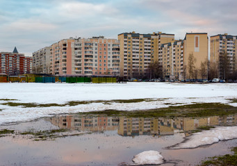 Fototapeta na wymiar Urban houses and sky with clouds reflected in puddle from melting snow on street in sunny spring day