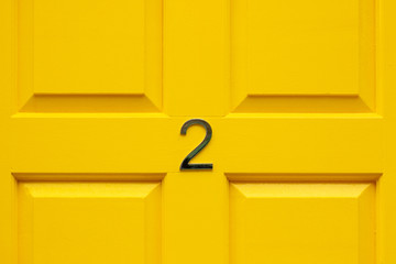 House number two with the 2 in the middle cross bar of a bright yellow painted house door