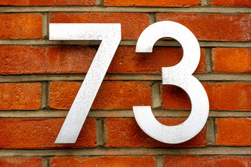 House number 73 with the seventy-three in silver on a red brick wall 
