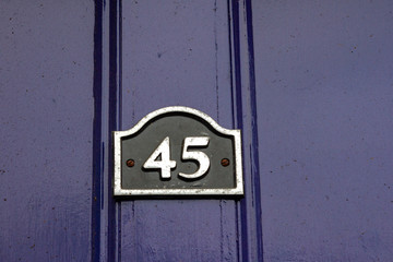 House number 45 with the forty-five on a black enamel sign on a dark blue almost purple house door 