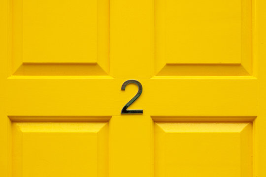 House number two with the 2 in the middle cross bar of a bright yellow painted house door