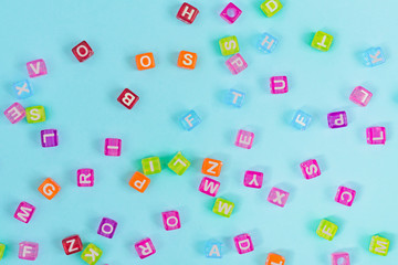 Multicolored plastic cube beads with letters scattered on blue background. Alphabet background texture.